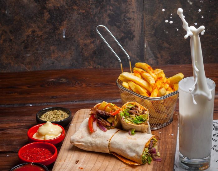 Side view shawarma with fried potatoes and ayran and splash in board cookware on stone background